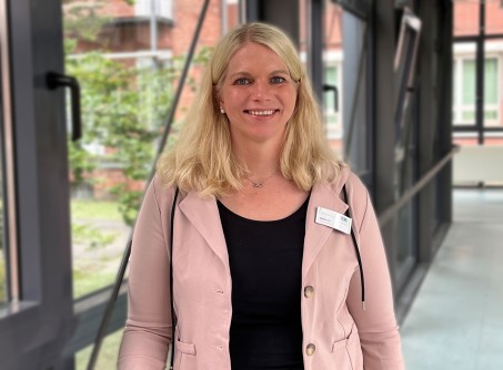 Blonde Frau mit hellblauem Hemd lächelt in die Kamera