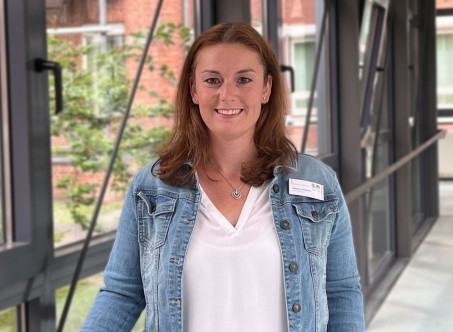 dunkelhaarige Frau steht vor einem Fenster und lächelt in die Kamera