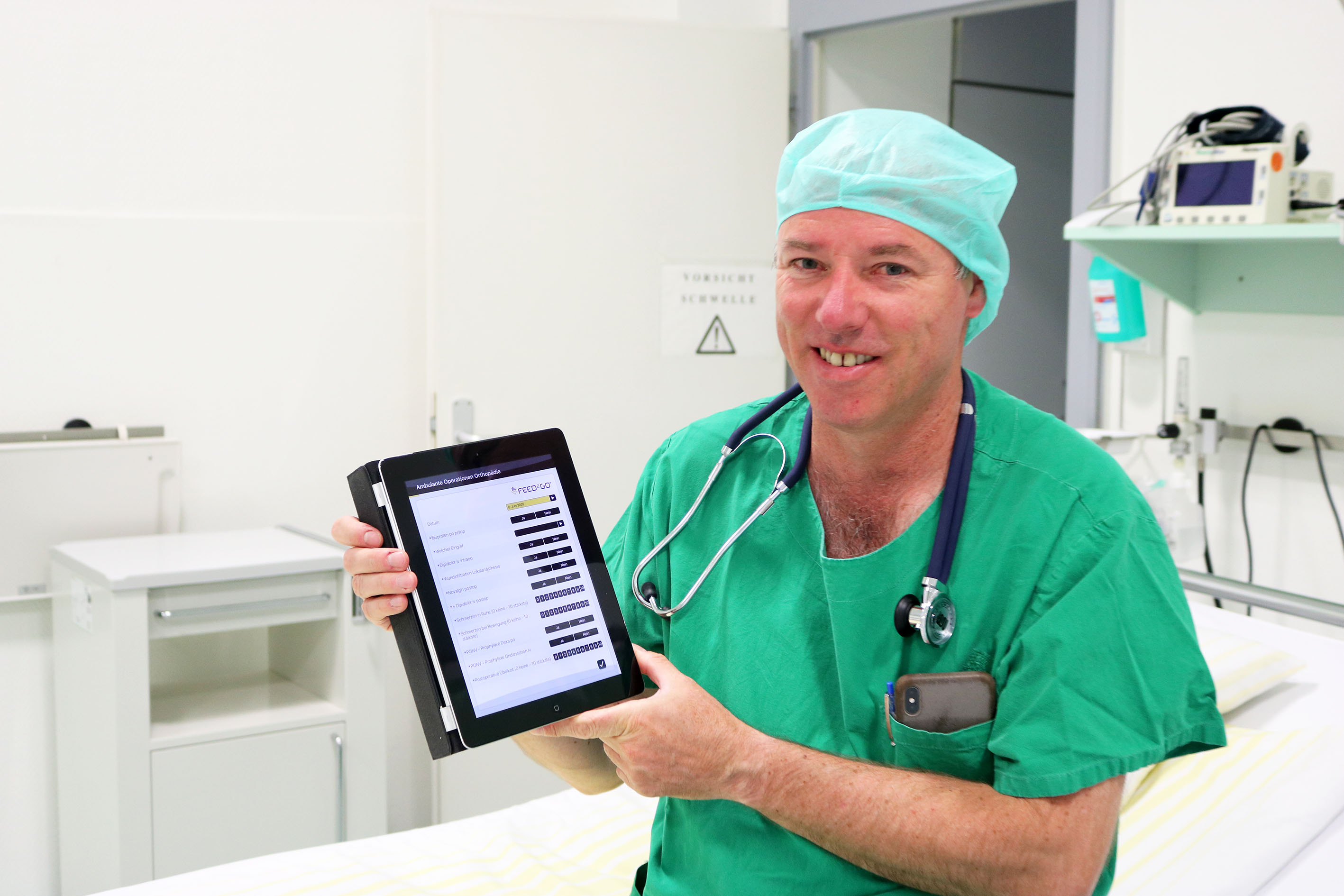 Leitender Anästhesist mit iPad in der Hand. Darauf ist der Patientenfragebogen zu sehen.