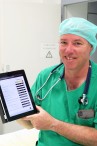 Leitender Anästhesist mit iPad in der Hand. Darauf ist der Patientenfragebogen zu sehen.